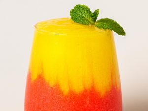 Strawberry mango margarita layered in a glass topped with mint leaves.