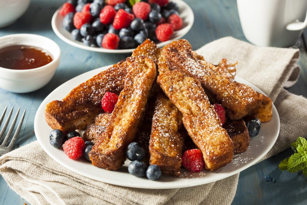 Plate of cinnamon-flavored French toast sticks, garnished with powdered sugar, fresh blueberries, and fresh raspberries