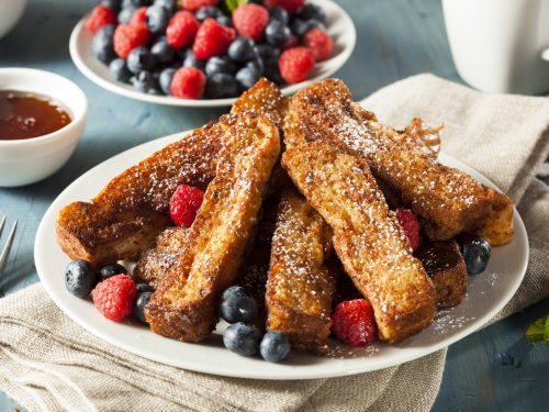 Plate of cinnamon-flavored French toast sticks, garnished with powdered sugar, fresh blueberries, and fresh raspberries