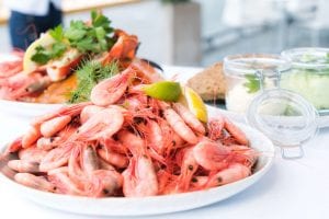a plateful of shrimps with slices of lemon on top, plateful of seafoods in the background