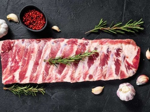 a rack of fresh spare ribs with herbs, spices, and seasonings on the background