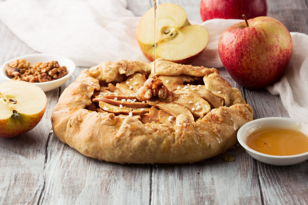 homemade crostata with ripe apples, nuts and maple syrup on rustic white wooden background, selective focus