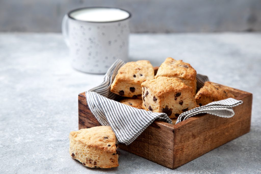 chocolate chip scones in a wooden box, a mug of milk on a gray background