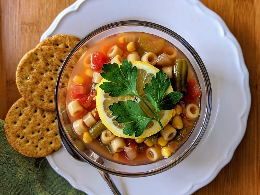 a top view of minestrone soup bowl garnished with lemon with biscuits on the side, pasta