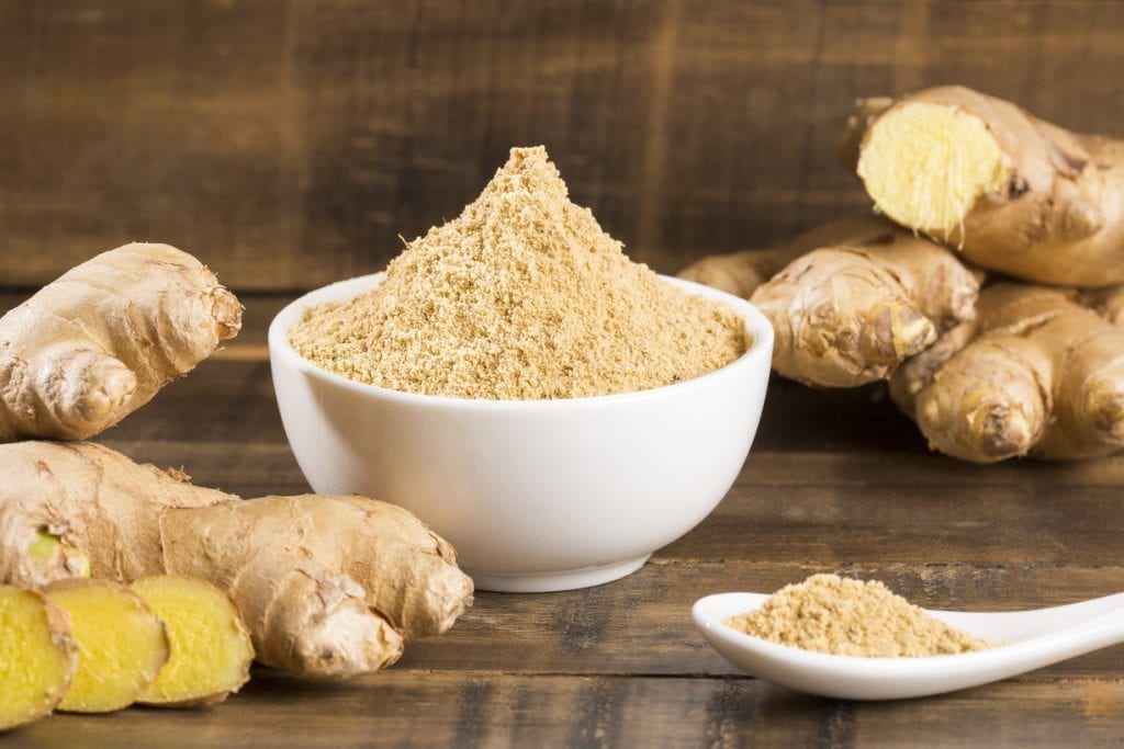 ground ginger in a small bowl with ginger roots in the background
