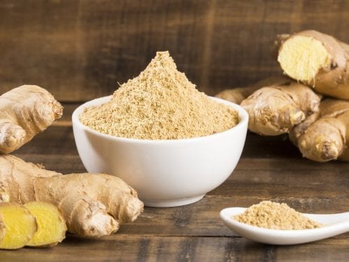 ground ginger in a small bowl with ginger roots in the background