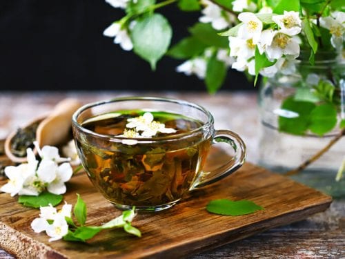 cup filled with jasmine green tea, jasmine flower petals