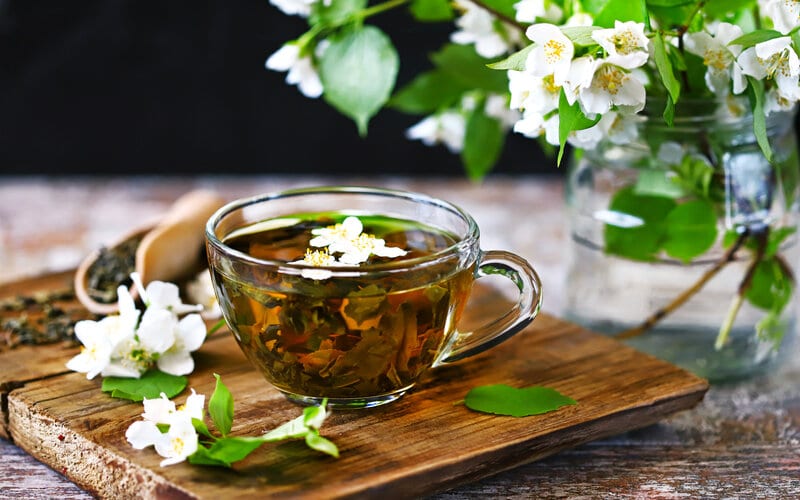 cup filled with jasmine green tea, jasmine flower petals