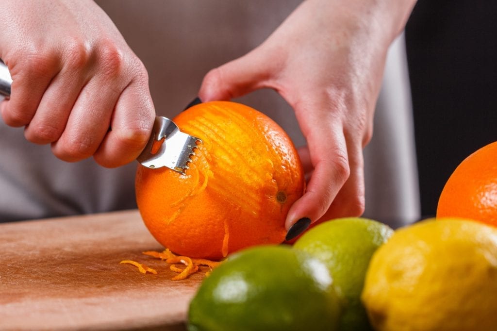 Person zesting an orange using a zester tool