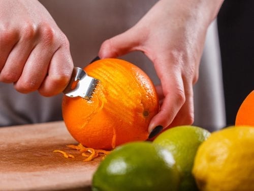 Person zesting an orange using a zester tool
