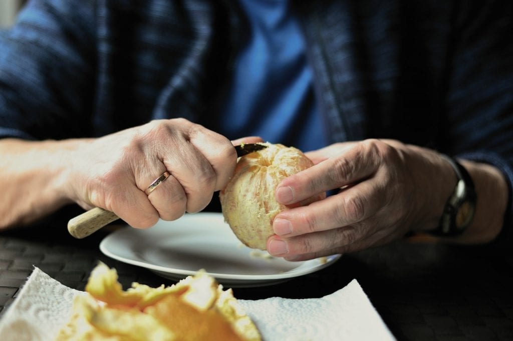 Person peeling an orange with a paring knife