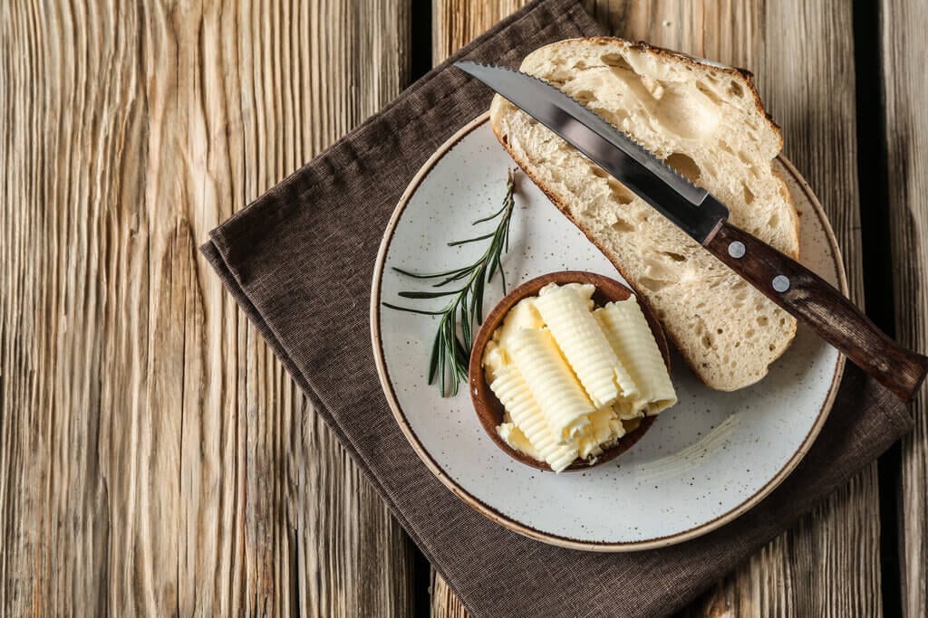 a piece of bread on plate, with butter curls and a serrated knife