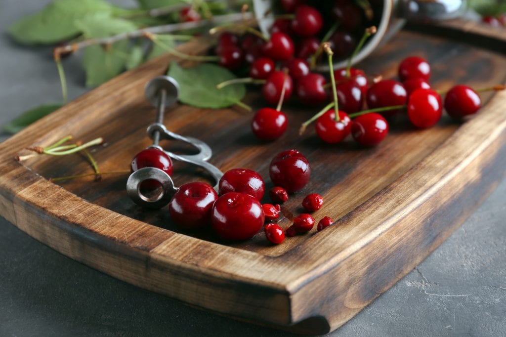 Metal cherry pitter with cherries on a wooden board