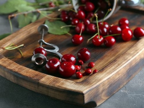 Metal cherry pitter with cherries on a wooden board
