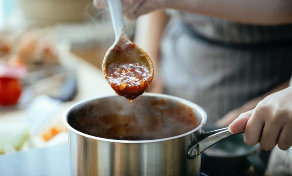 Person scooping sauce with a wooden spoon from a saucepan