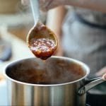 Person scooping sauce with a wooden spoon from a saucepan