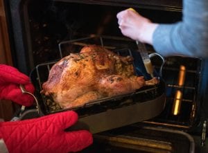 Two people preparing roast turkey with a tube turkey baster