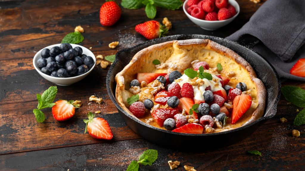 Dutch baby pancake with mixed berries and icing sugar in a cast iron pan.