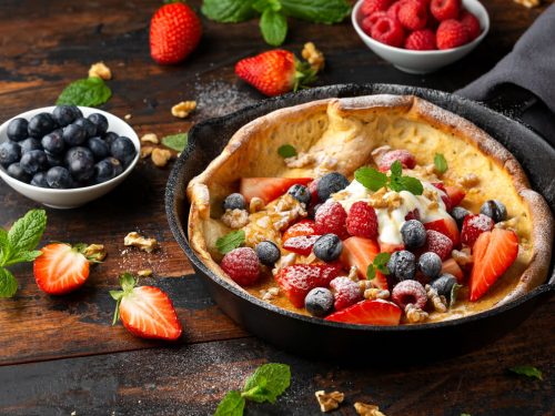Dutch baby pancake with mixed berries and icing sugar in a cast iron pan.