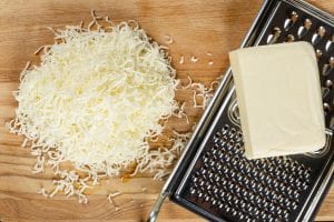 top view of grated mozzarella cheese, slab of cheese, and metal cheese grater
