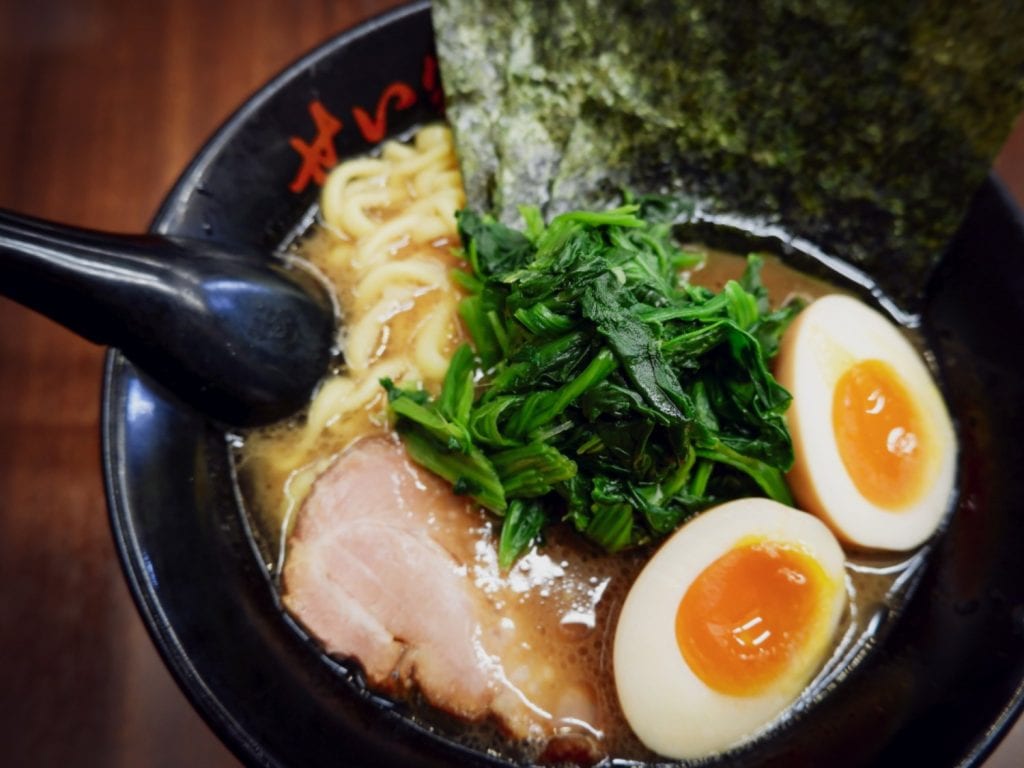 Bowl of noodle soup with ramen toppings including ajitama, aonegi, nori, and chashu