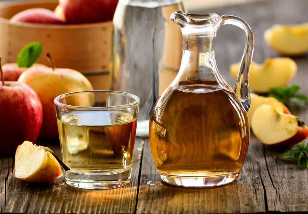 a glass and bottle of apple cider vinegar with apples