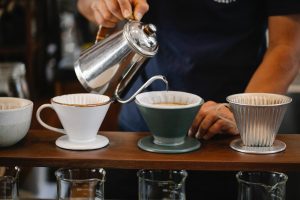 Person pouring water to a cup from a metal gooseneck kettle