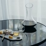 Red wine in a glass decanter, with a stemless wine glass and charcuterie on the side
