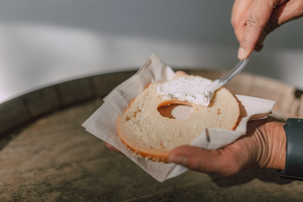 Person spreading cream cheese on a halved bagel