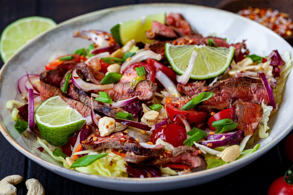 thai beef salad with vegetables and nuts in a white bowl