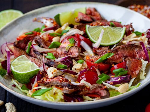 thai beef salad with vegetables and nuts in a white bowl