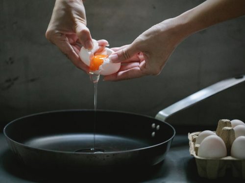 person cracking open an egg over pan, different ways to cook eggs