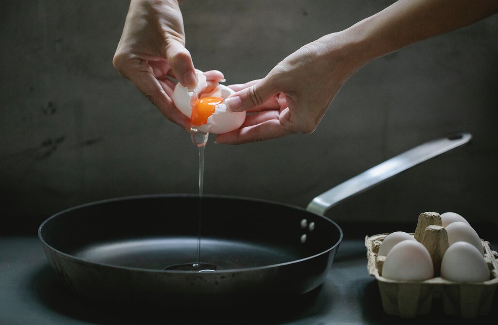 person cracking open an egg over pan, different ways to cook eggs