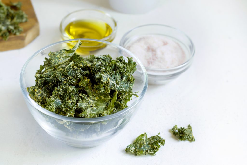 Crispy kale chips in a transparent glass bowl, with condiments on the side