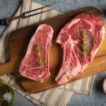 Raw piece of New York strip vs ribeye on a wooden board