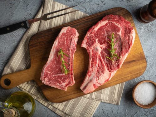 Raw piece of New York strip vs ribeye on a wooden board