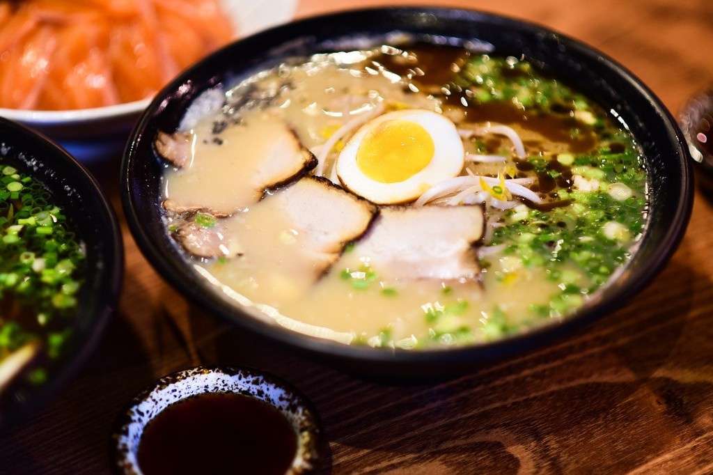 Bowl of paitan or white broth ramen, with halved soft-boiled egg, chashu, chopped green onions, and brown sauce on top