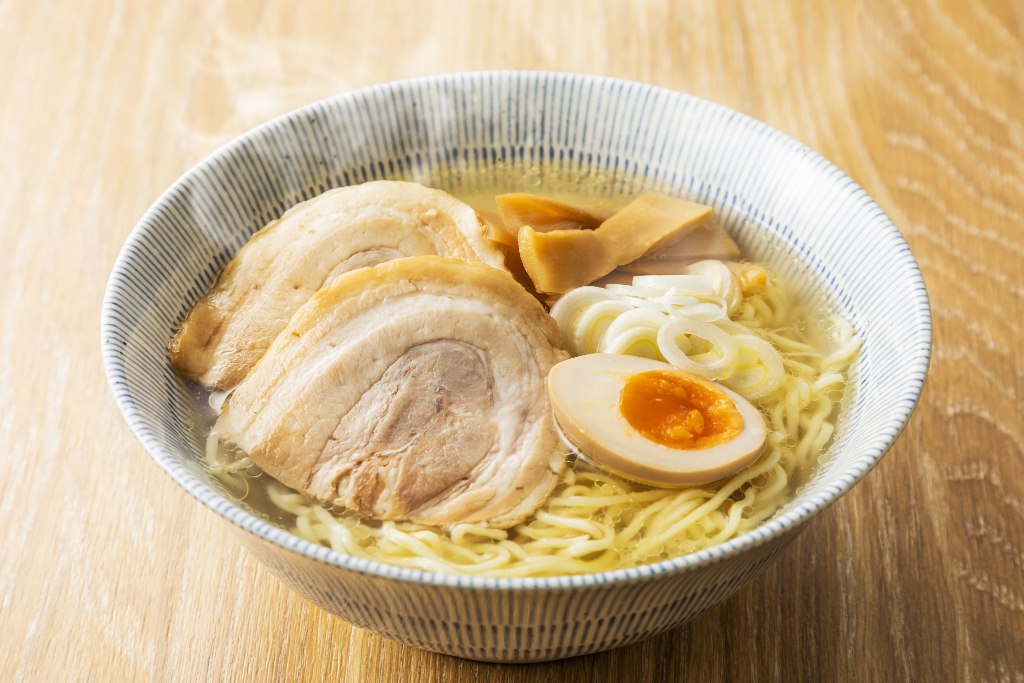 Bowl of shio ramen: noodles in clear broth and topped with chashu, fermented bamboo shoots, chopped scallions, and halved soft-boiled egg