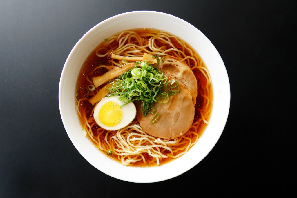 Shoyu ramen with clear brown broth and wavy noodles, topped with halved boiled egg, chashu, chopped scallions, fermented bamboo shoots