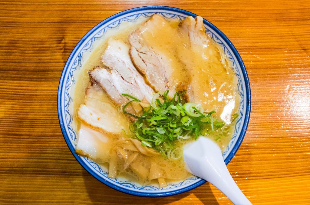 Bowl of Fukuoka tonkotsu ramen with cloudy pork bone broth, topped with chashu slices, chopped scallions, and fermented bamboo