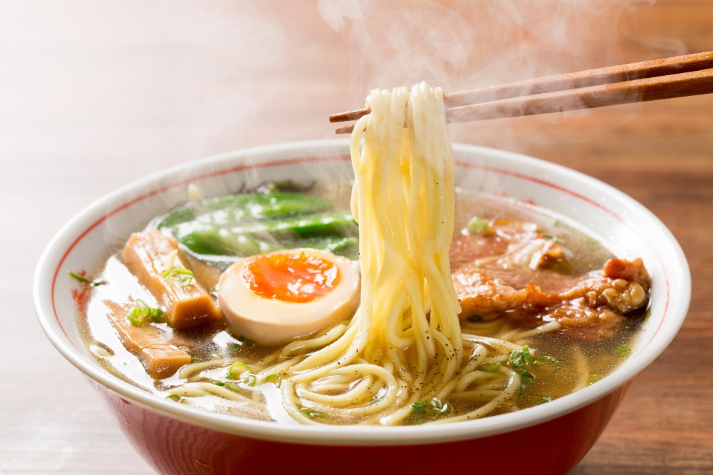 Bowl of shoyu ramen, one of the many types of ramen, with clear broth, straight noodles, halved soft-boiled egg, fermented bamboo shoots, meat, and vegetables