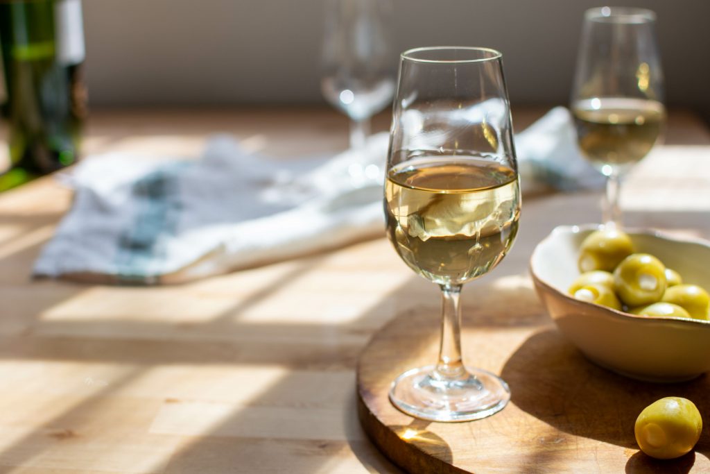 two glass of dry sherry wine, olives in a bowl, and an empty glass on top of a wooden table