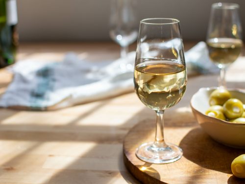 two glass of dry sherry wine, olives in a bowl, and an empty glass on top of a wooden table