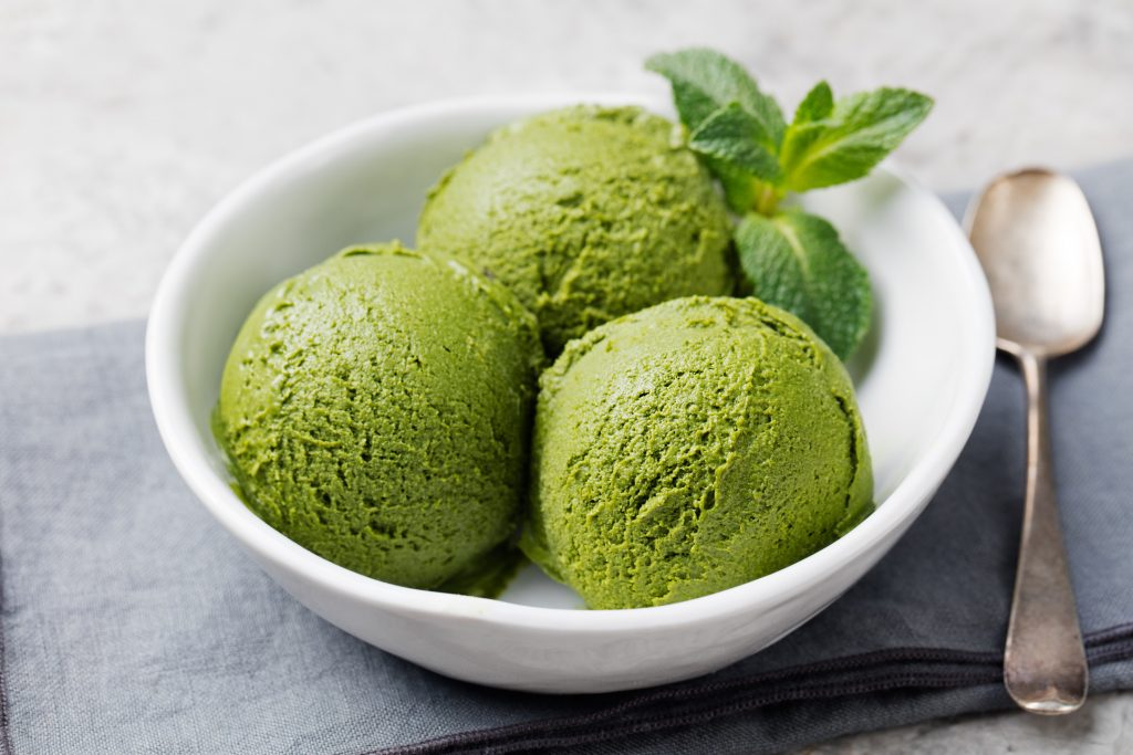 Green tea matcha ice cream scoop in white bowl on a grey stone background.