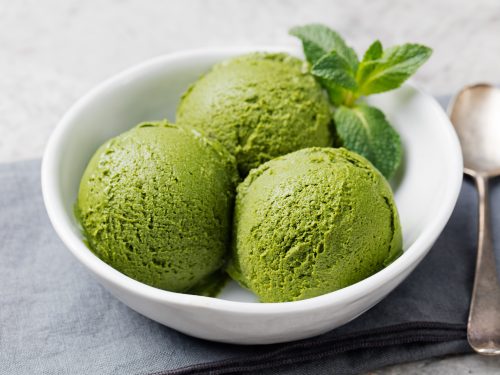 Green tea matcha ice cream scoop in white bowl on a grey stone background.