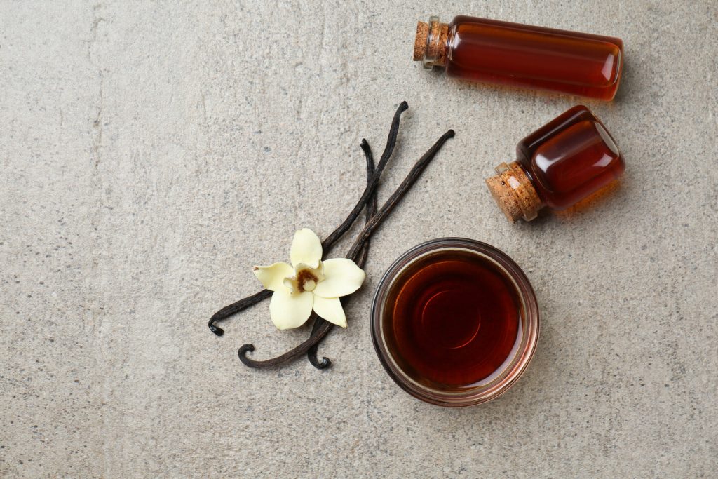 glass and bowls of vanilla extract on a gray background