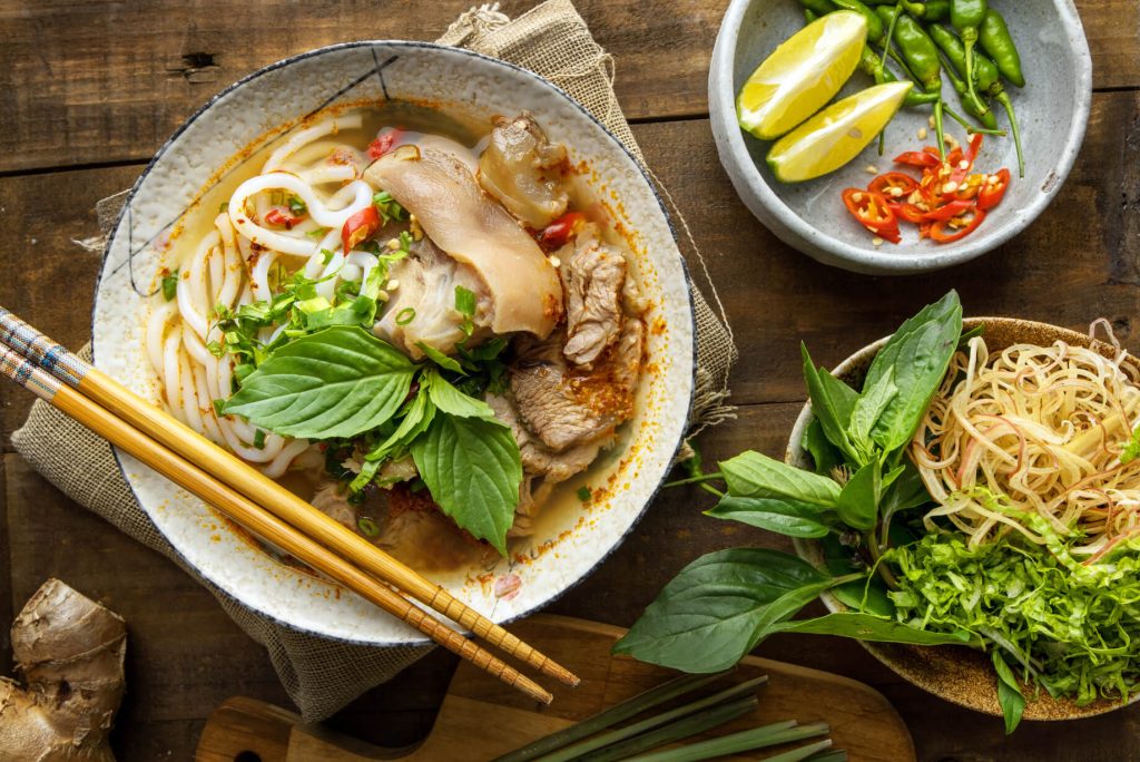 bun bo hue on a white bowl, lemon, red chilis, and fresh herbs