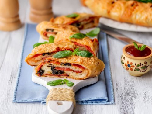 stromboli vs calzone, sliced italian stromboli stuffed with salami, cheese, black olive and tomato sauce on table