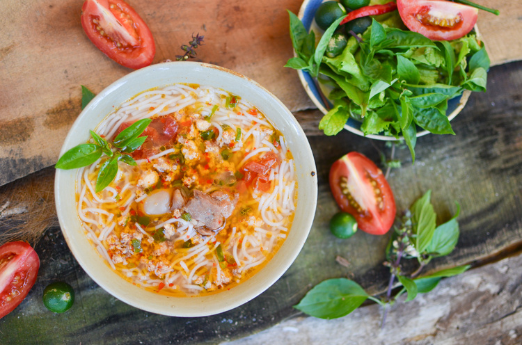 bun rieu in a white bowl with tomatoes and fresh veggies