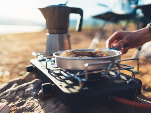 person preparing breakfast on a camp stove, easy camping breakfast ideas